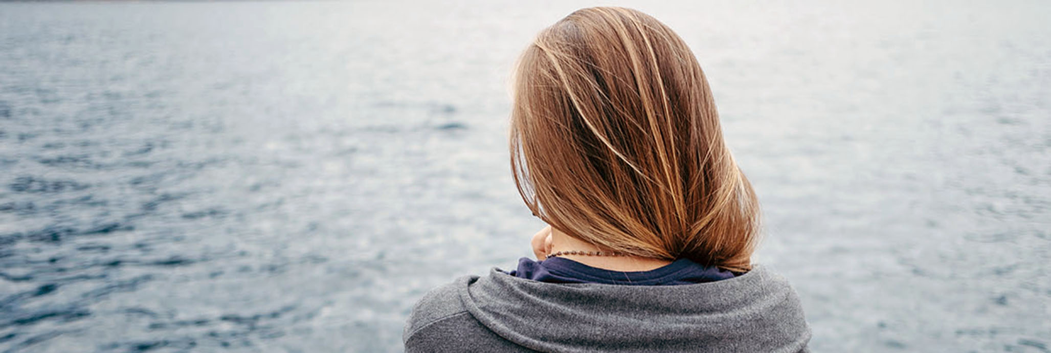 En person sedd bakifrån står och tittar ut över vattnet.