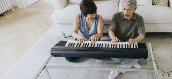 En äldre man och en äldre kvinna sitter på golvet och spelar keyboard.