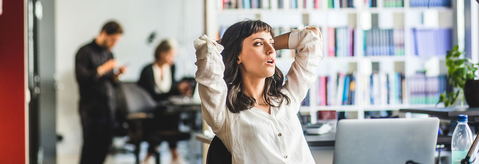 En person i ett kontorslandskap lutar sig bak i en kontorsstol. Hon har munnen öppen och tittar ut i fjärran.