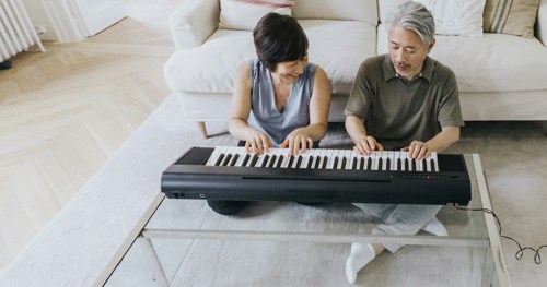 En äldre man och en äldre kvinna sitter på golvet och spelar keyboard.